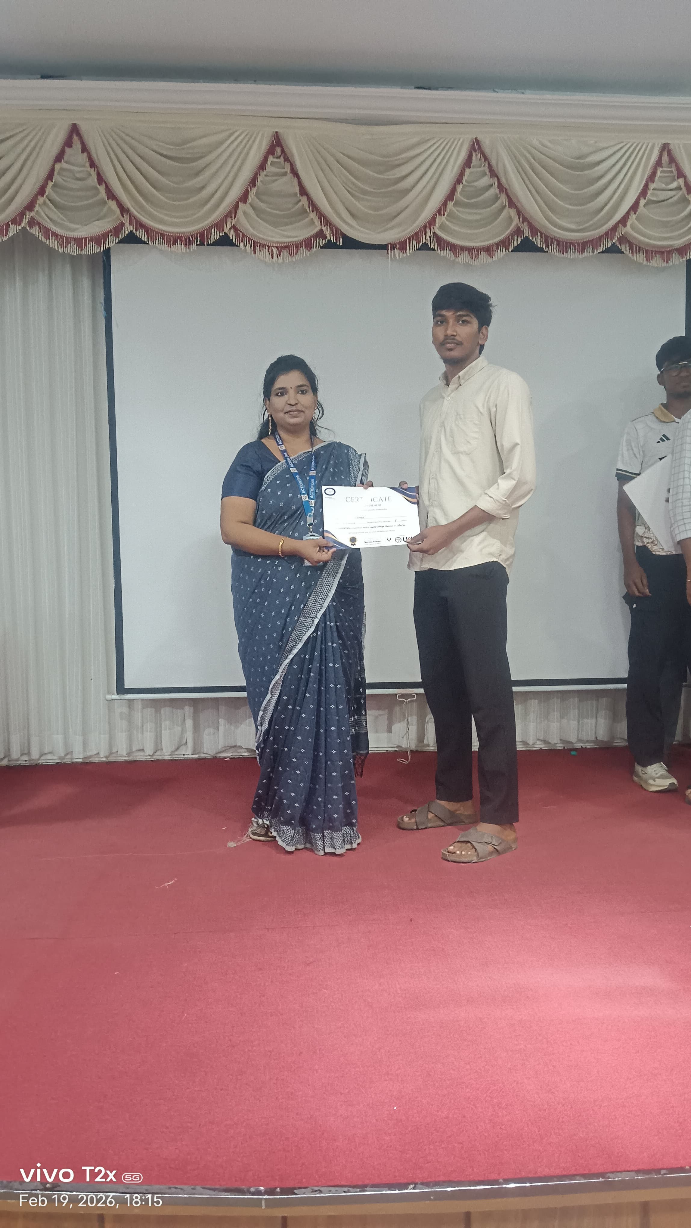 Trainer presenting a certificate to a student on a college auditorium stage