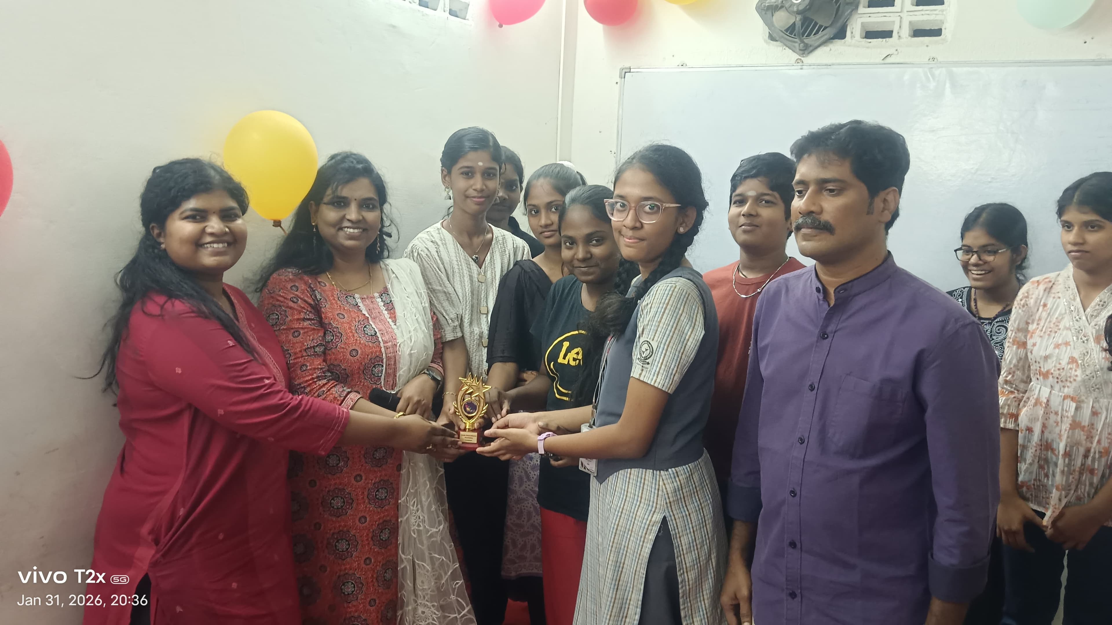 Students and facilitators holding a trophy together at a balloon-decorated event
