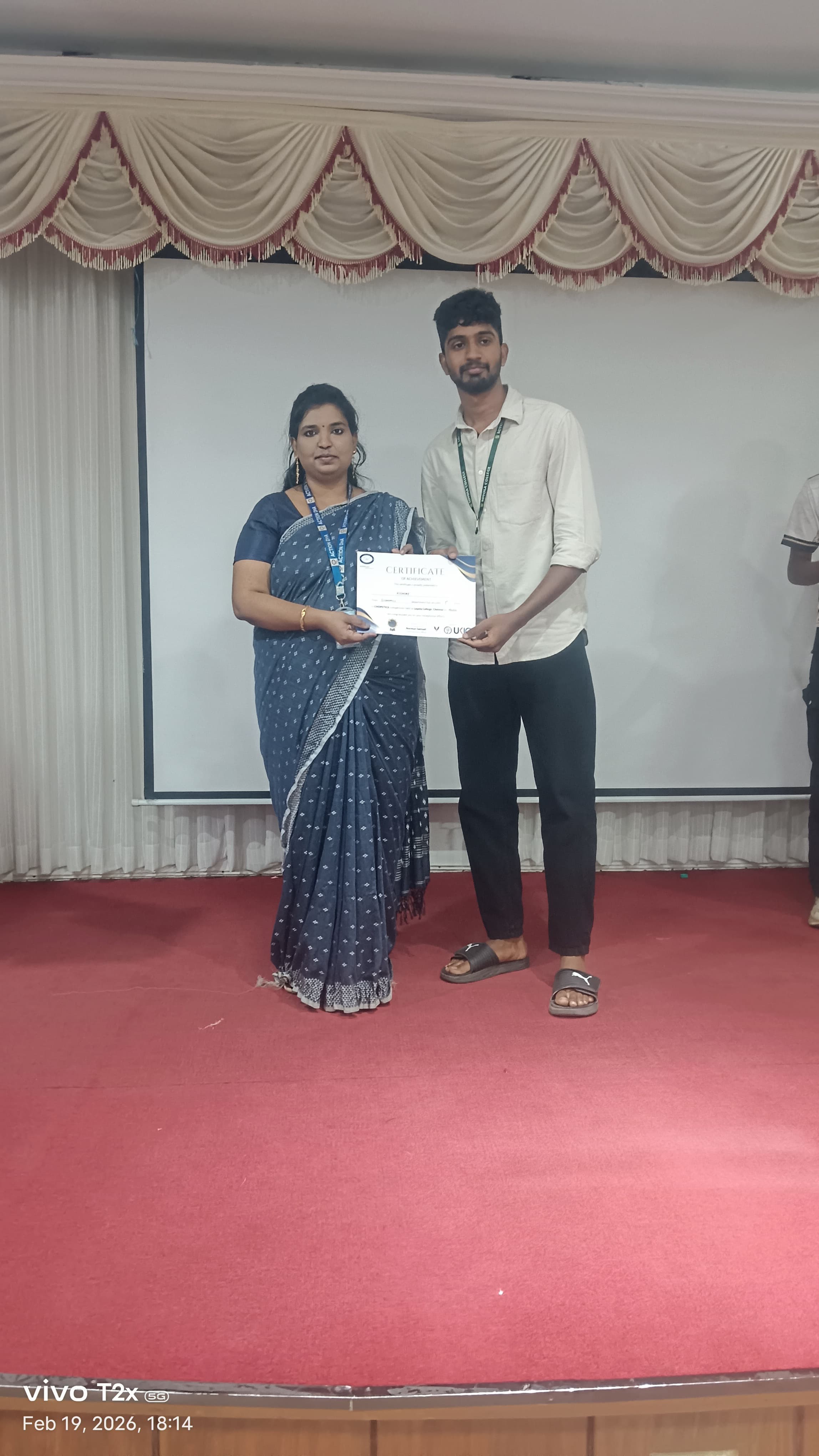 Facilitator presenting a certificate to a student on a college auditorium stage