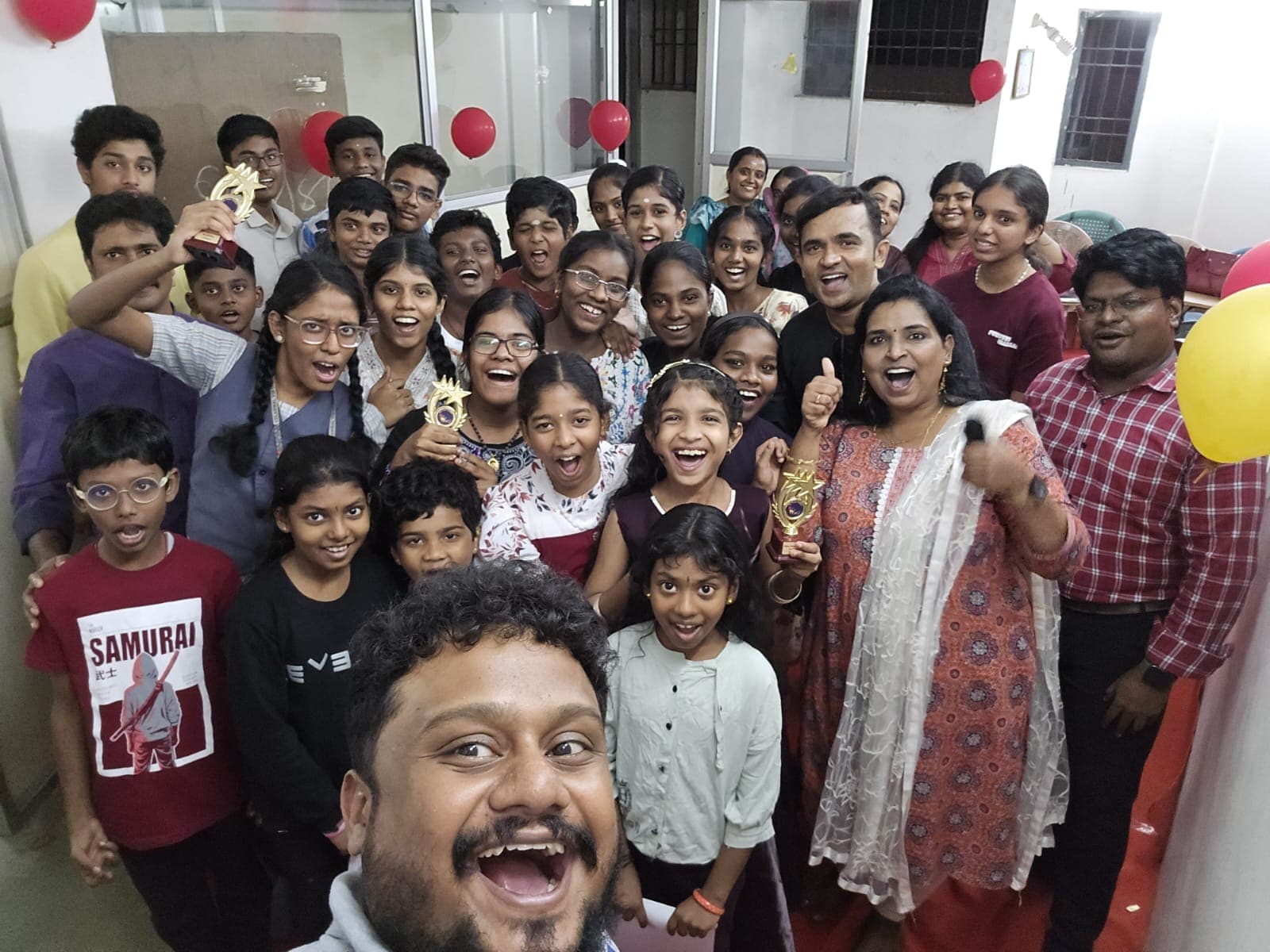 Large group selfie with trophies at a balloon-decorated celebration