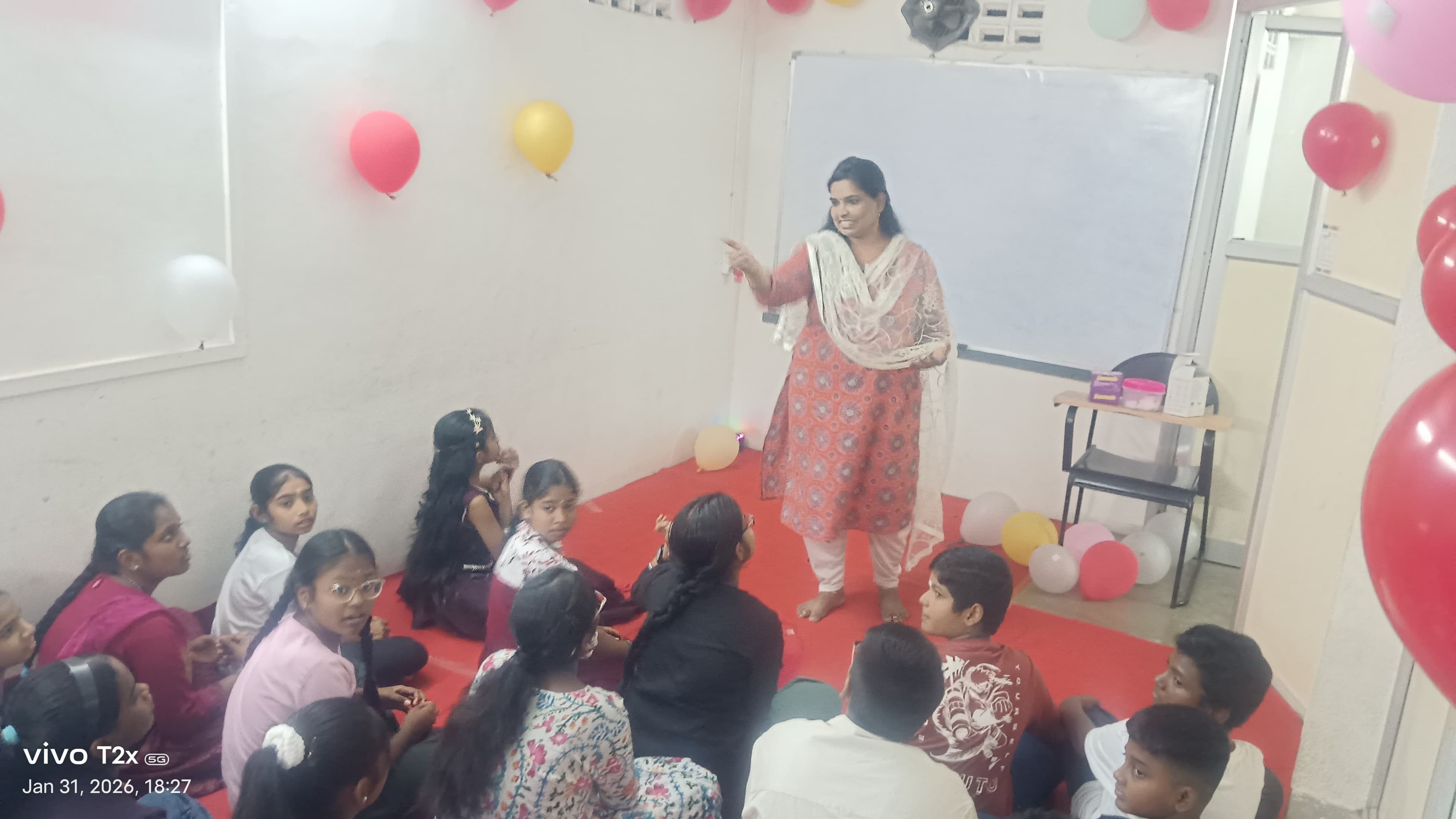 Facilitator addressing a group of children seated on the floor at a balloon-decorated event