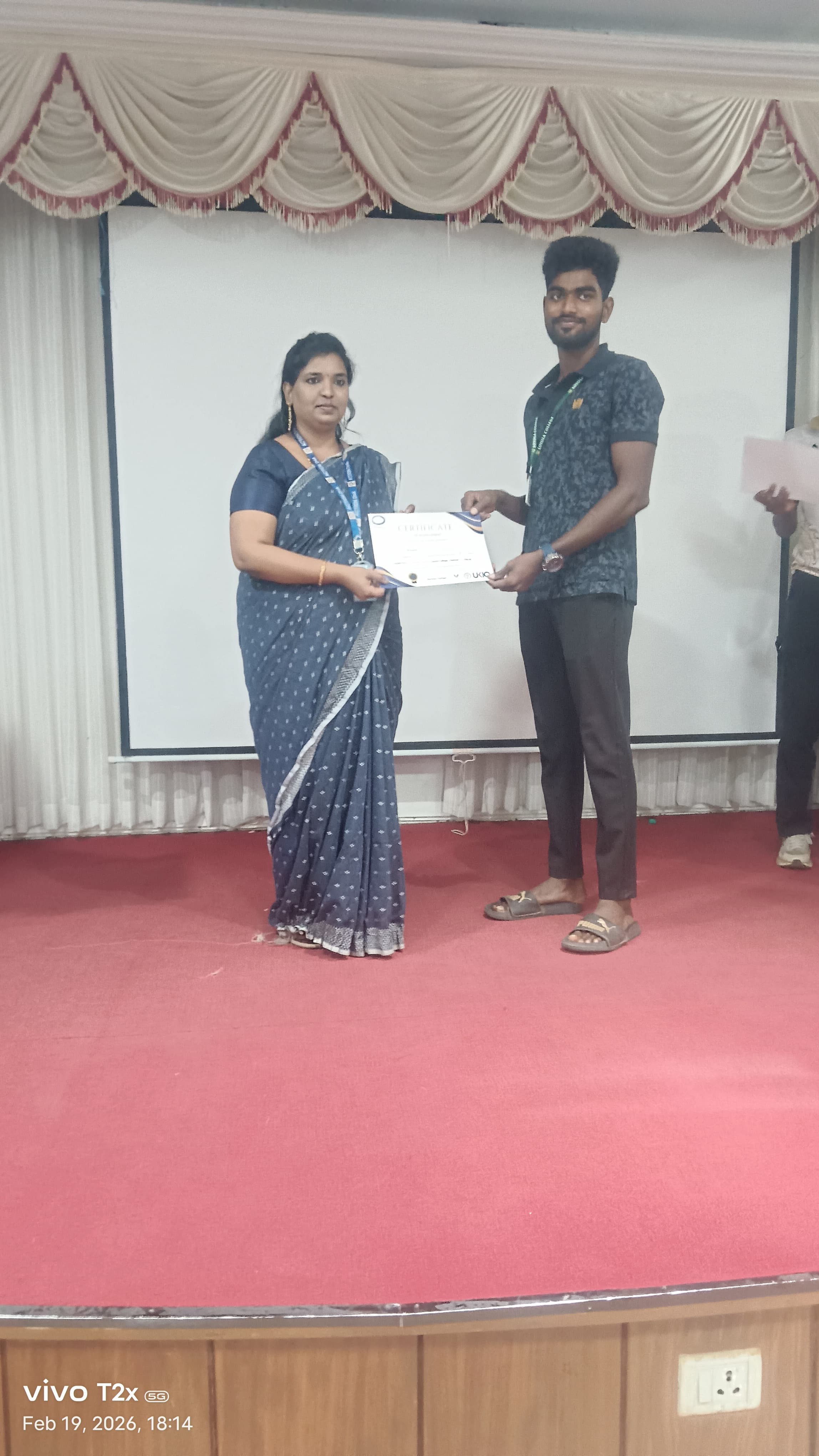 Facilitator presenting a certificate to a student on a college auditorium stage