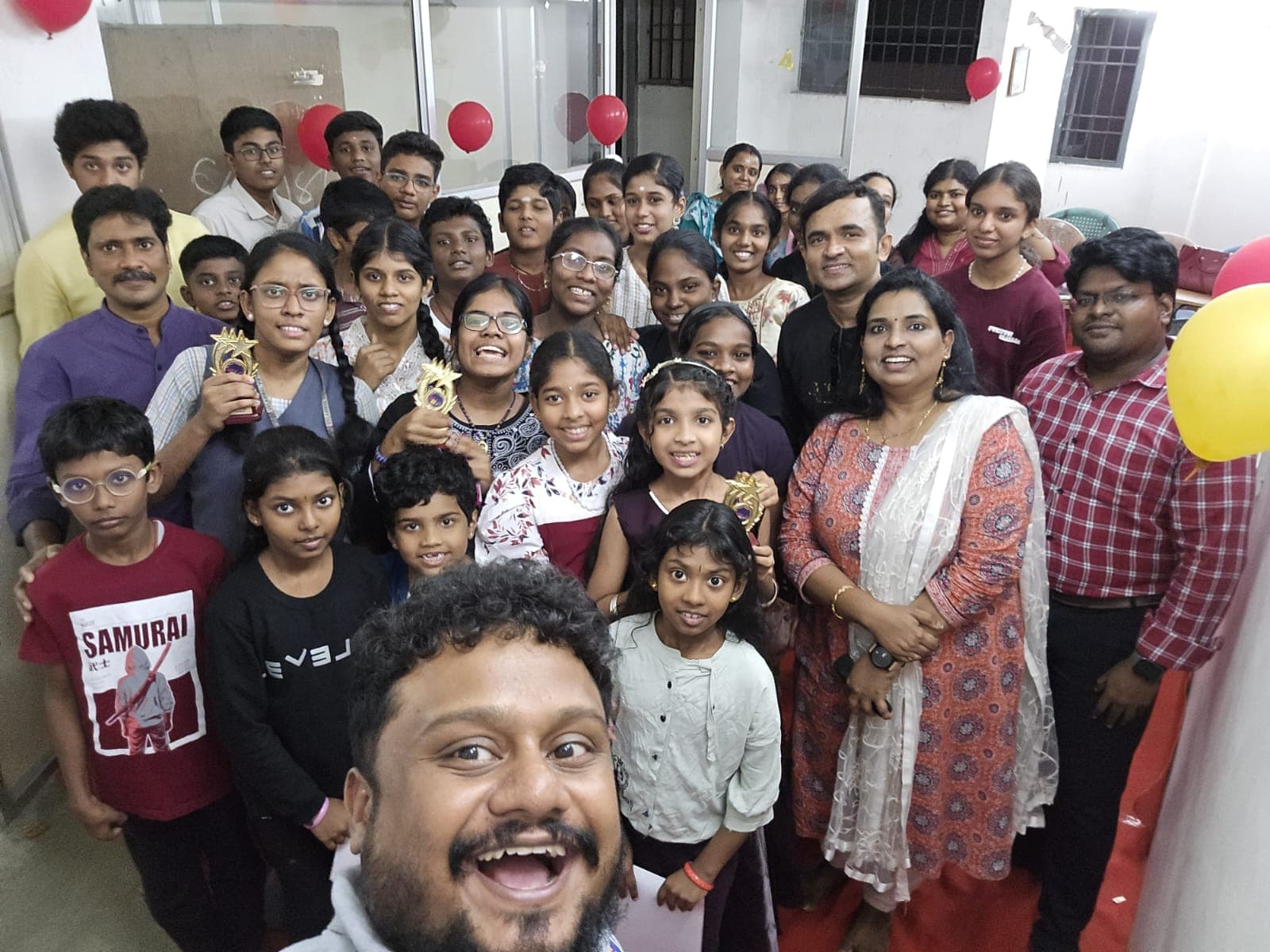 Large group photo at a celebration with balloon decorations and trophies