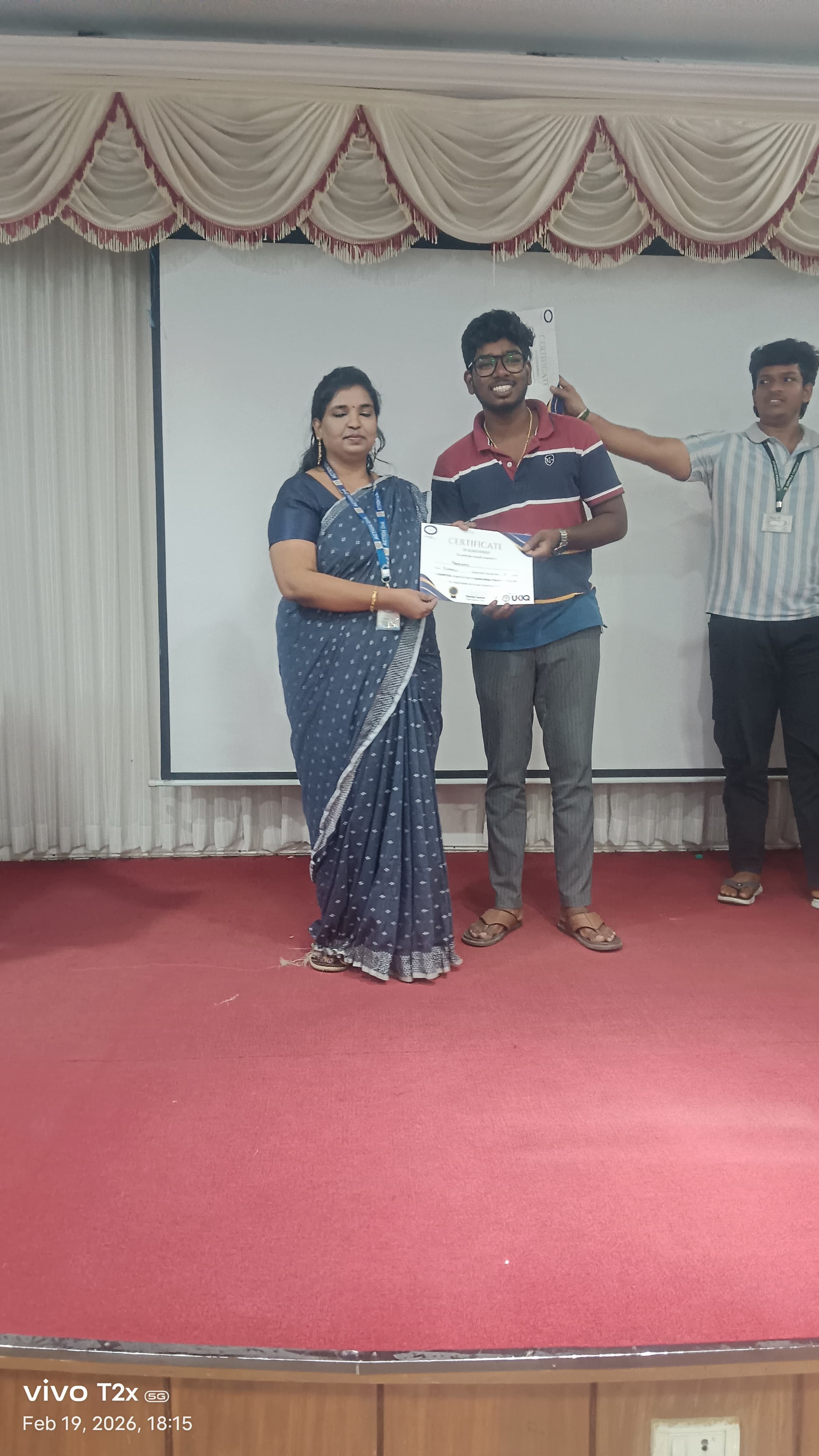 Facilitator presenting a certificate to a student on a college auditorium stage