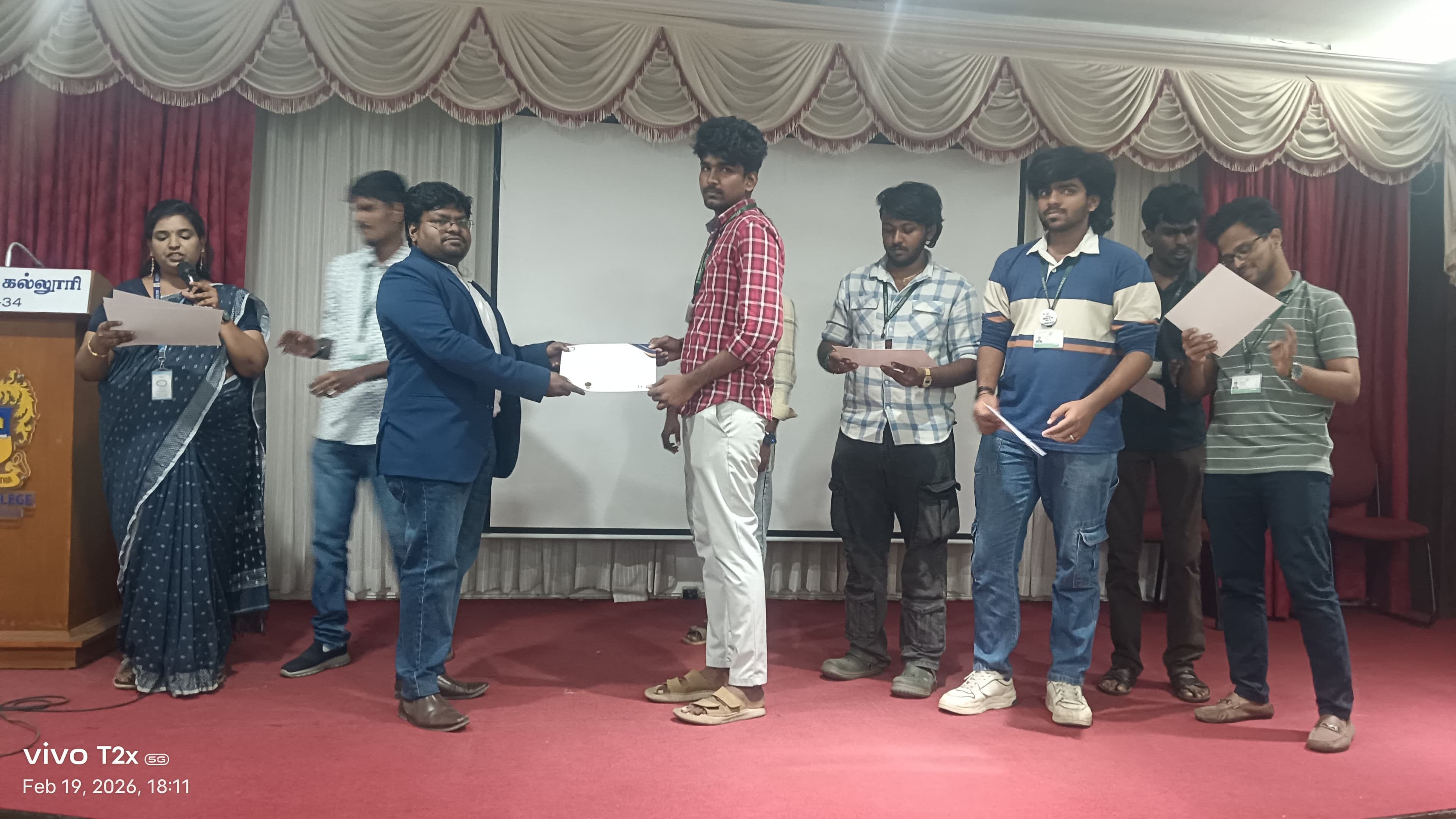 Facilitator presenting a certificate to a student on a college auditorium stage