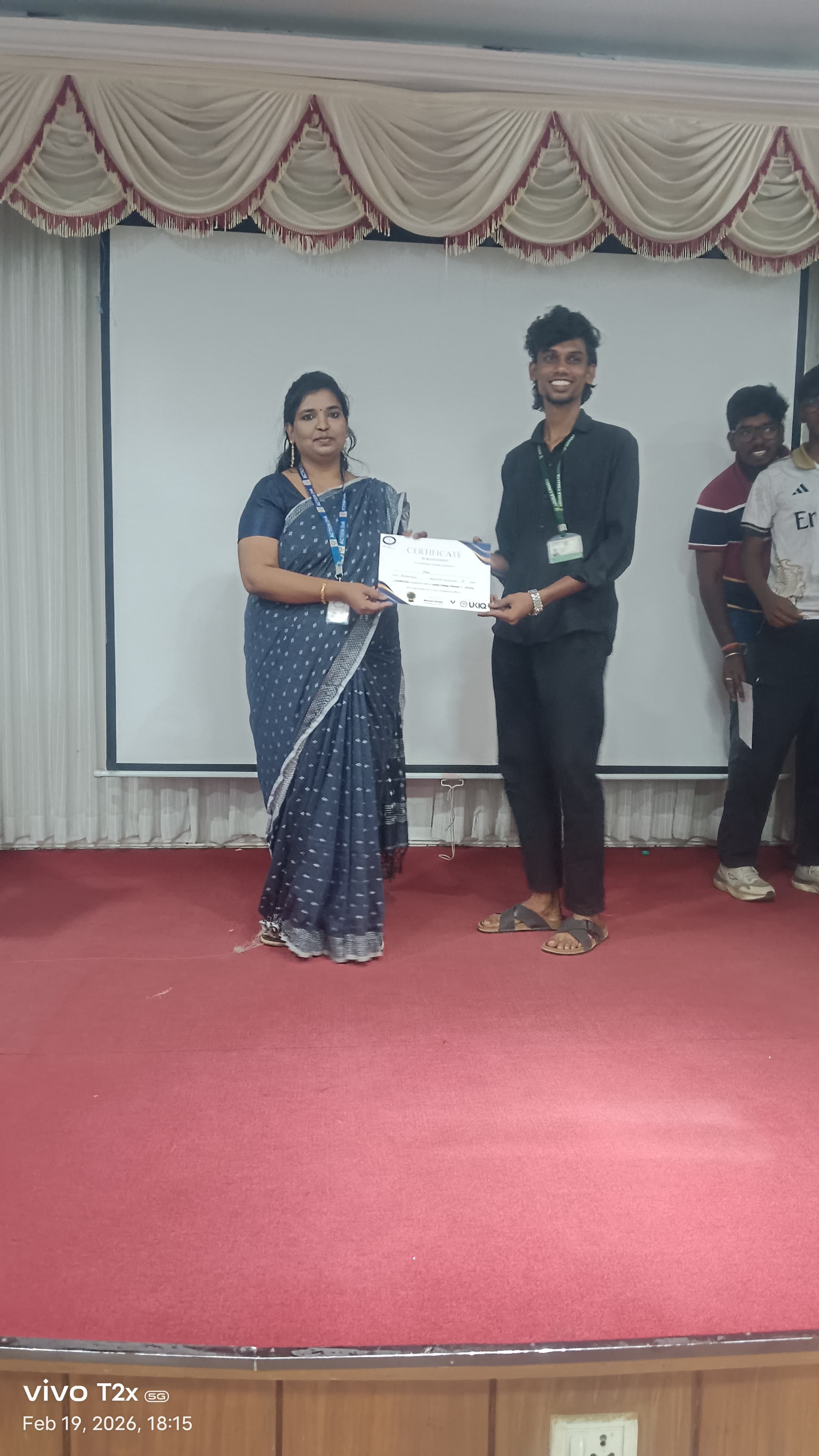 Facilitator presenting a certificate to a student on a college auditorium stage
